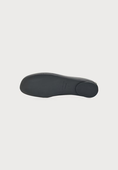 Semelle de chaussure plate noire avec bout arrondi et petit talon, présentée sur un fond blanc uni.
