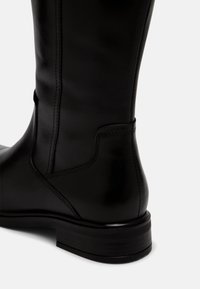 Černá kožená vysoká bota s hladkým povrchem, prošívanými detaily a nízkým zpevněným podpatkem, s elegantním a štíhlým designem.