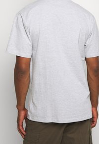Camiseta de algodón gris, de manga corta, cuello redondo, diseño liso, ligera textura visible, usada con pantalones cortos de carga verdes, vista desde atrás.