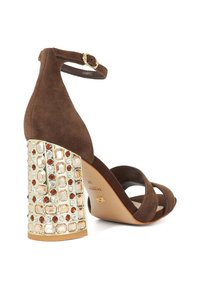 Brown suede high-heeled sandal with a decorative embellished block heel featuring clear and colored gems. Adjustable ankle strap included.