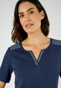 Póloa azul marino con mangas cortas y un escote en V, con acentos a rayas en los hombros. Material suave con una textura lisa.