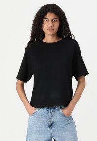 Svart T-skjorte med korte ermer laget av mykt stoff, med en avslappet passform og rund halslinning, båret med høyt liv lyseblå jeans.