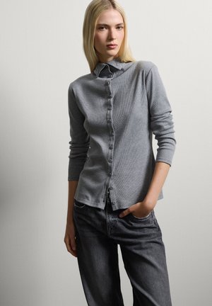 Cardigan grigio con bottoni, a maniche lunghe, realizzato in tessuto texture. Dotato di colletto e bottoni sul davanti, abbinato a jeans scuri.