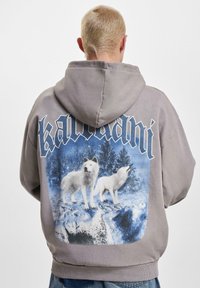 Gray hoodie featuring a graphic of two white wolves on a snowy landscape, with the word "karmani" printed above in dark blue stylized font.