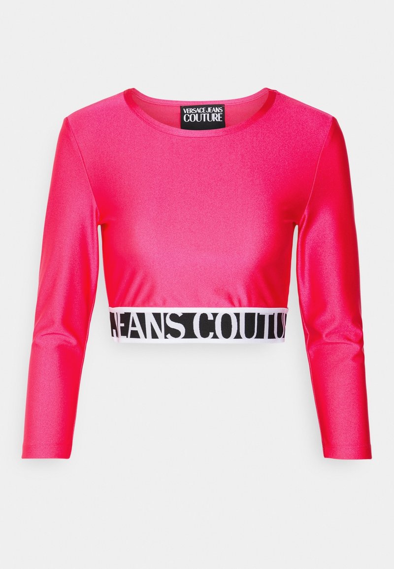 Kirkkaan vaaleanpunainen lyhyt toppi pitkillä hihoilla, valmistettu kiiltävästä materiaalista. Helma on varustettu mustavalkoisella joustovyöllä, jossa on teksti "JEANS COUTURE".