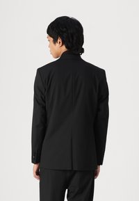 Black blazer featuring a tailored cut, clean lines, and a smooth texture, with a single back vent and button accents on the sleeves.