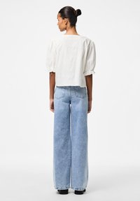 Top ivory scurt cu mâneci bufante și decolteu pătrat, asortat cu blugi din denim ușor, cu croială largă, având buzunare pe spate și tiv brut.