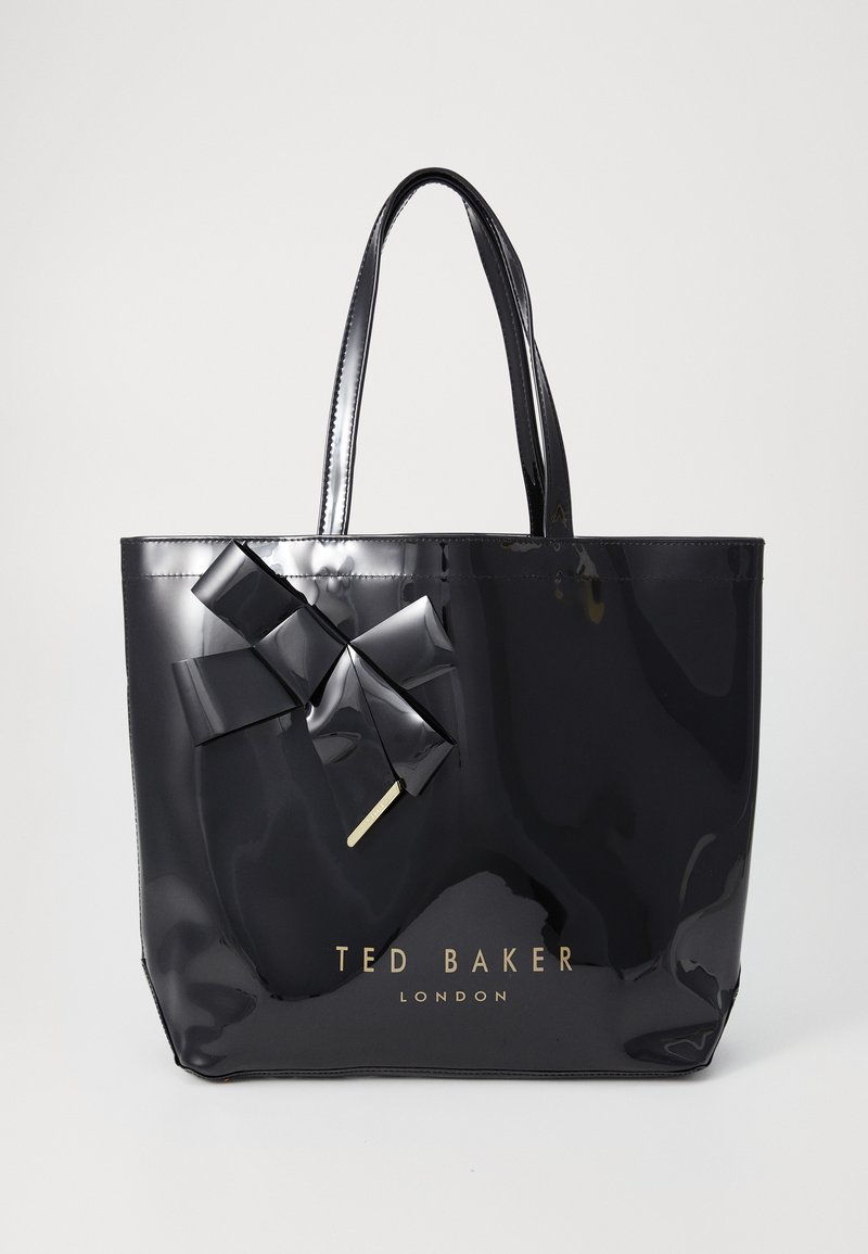 Svart lackad tote-väska med glänsande yta, prydd med en stor satängrosett och gyllene branding. Dubbelhandtag för enkel bärning.