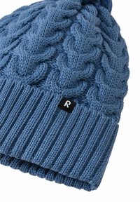 Niebieska dziana czapka z warkoczowym wzorem, prążkowanym mankietem i małą czarną metką z białą literą "R" na mankiecie.