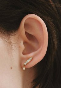 Pendientes de oro con forma ovalada que presentan cinco piedras transparentes y una piedra en forma de pera más pequeña colgando por debajo. Acabado texturizado.