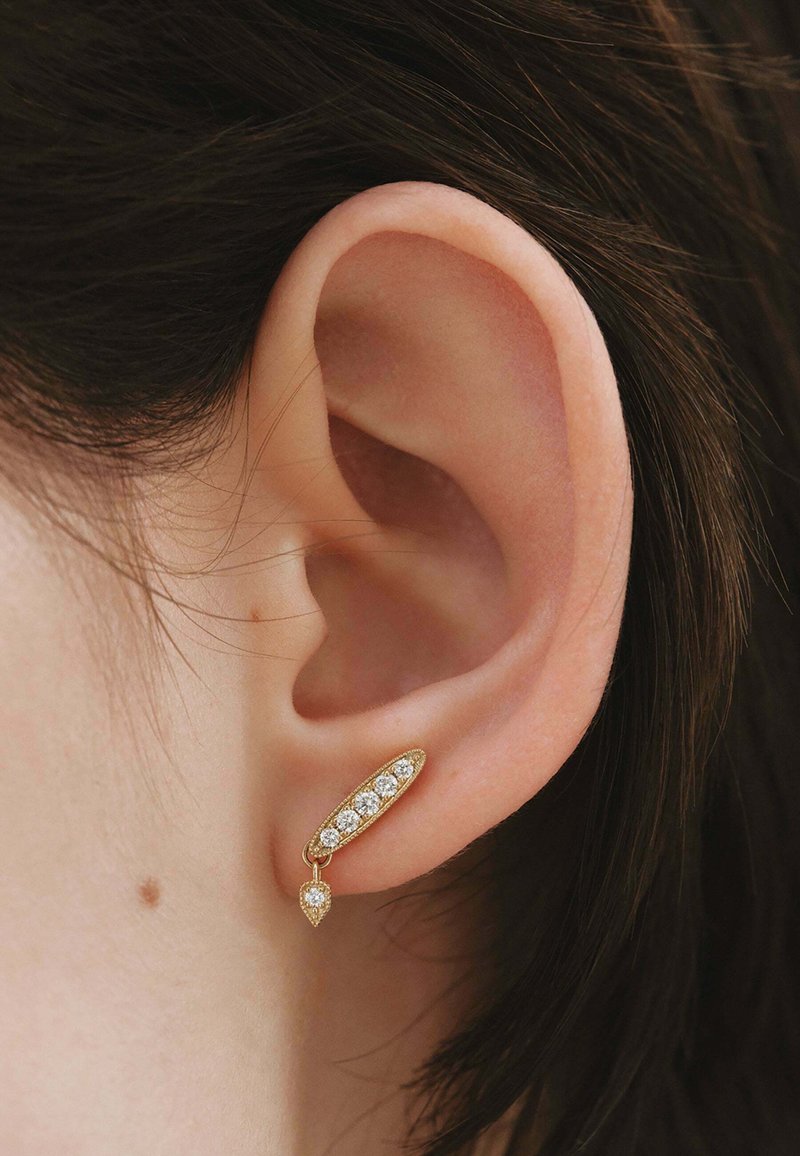 Pendientes de oro con forma ovalada que presentan cinco piedras transparentes y una piedra en forma de pera más pequeña colgando por debajo. Acabado texturizado.