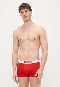 Sarkanas kokvilnas bokseršorti ar baltu jostasvietu, uz kuras ir Diesel logotips, gluda tekstūra un pieguļošs dizains.