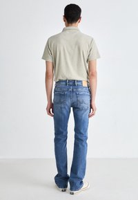 Camisa polo en gris claro con cuello, combinada con unos vaqueros de denim azul con un desgastado ligero y bolsillos traseros bordados. Parche de logo visible.