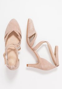 Zapatos de tacón de ante nude con punta afilada, tiras alrededor del tobillo y un tacón de 6.5 cm. Presentan un interior suave y tiras entrelazadas para mayor soporte.