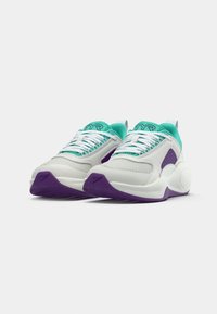 Białe sneakersy z turkusowymi akcentami i fioletowymi podeszwami. Charakteryzują się siateczkowymi panelami, wyściełanym kołnierzem oraz białymi sznurówkami, zapewniającymi pewne dopasowanie.