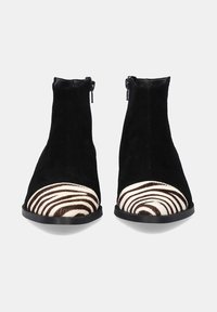Botines de ante negros con una puntera de pelo a rayas marrón y blanca. Presentan cremalleras a ambos lados y una suela negra plana.