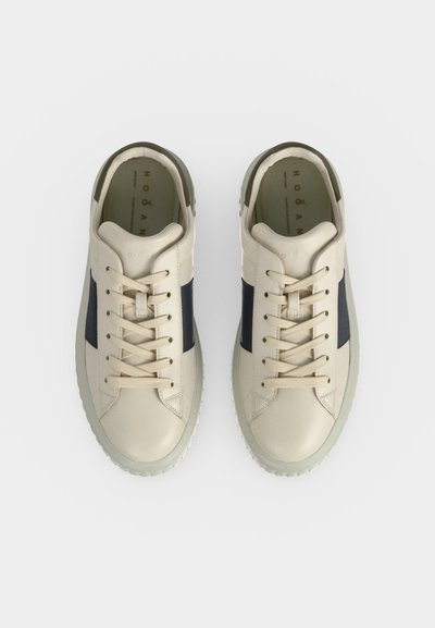 Paire de baskets en cuir écru avec des panneaux latéraux foncés, lacets noués, vues de dessus sur un fond clair uni.