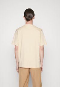 Beige kortärmad t-shirt i bomull med rund nacke och avslappnad passform, visad framifrån mot en enkel bakgrund.