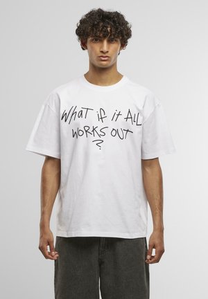 Weißes Baumwoll-T-Shirt mit kurzen Ärmeln, das auf der Vorderseite mit einem großen, schwarz handgeschriebenen Textdesign mit der Aufschrift "Was, wenn alles gut wird?" versehen ist.