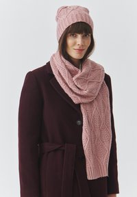 Roosa kudum müts ja sallikomplekt, millel on soonikmustri detail, kantud tumeda burgundia värvi mantliga. Sall ripub elegantselt kaela ümber.