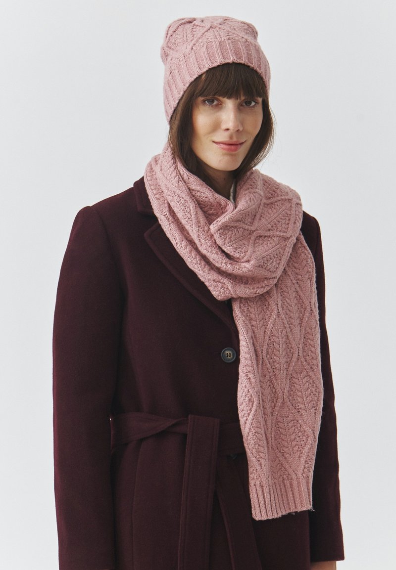 Roosa kudum müts ja sallikomplekt, millel on soonikmustri detail, kantud tumeda burgundia värvi mantliga. Sall ripub elegantselt kaela ümber.