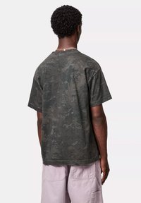 T-shirt bawełniany w ciemnozielonym kolorze z teksturowanym wzorem w stylu kamuflażu. Krótkie rękawy i luźny krój, z okrągłym dekoltem i prostym dołem.