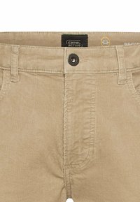 Beige Cordhosen mit strukturierter Oberfläche, ausgestattet mit einem schwarzen Knopfverschluss und normalen Taschen, entworfen für aktive Nutzung.