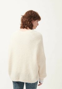 Cream-colored oversized knit sweater with a textured pattern, wide cuffs, and a scoop neckline, paired with blue denim jeans.