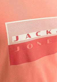 Tissu corail avec un graphisme à pois blancs et rouges comportant le texte « JACK & JONES » en lettres grasses.