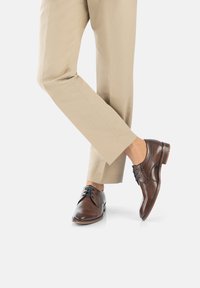 Souliers en cuir marron avec une finition lisse, présentant un laçage, un léger renfort au niveau des orteils et une semelle extérieure de couleur brune contrastante.
