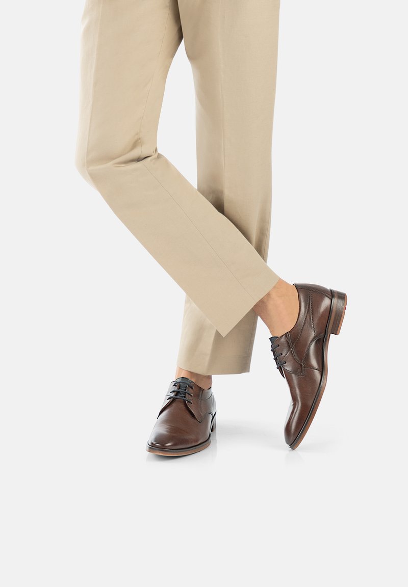 Souliers en cuir marron avec une finition lisse, présentant un laçage, un léger renfort au niveau des orteils et une semelle extérieure de couleur brune contrastante.