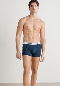 Navy plave Nike bokserice s elastičnim pojasom na kojem je prikazan logo branda. Napravljenje su od glatkog, rastezljivog materijala za udobnost.
