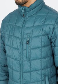 Teal pufferjakke med quiltet mønster, høj krave, frontlynlås og en lynlås-lukket brystlomme. Glat, skinnende stof med en let følelse.