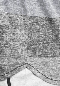 Grau farbige Blockhemd mit unterschiedlichen Grautönen und Texturen, mit einem abgerundeten Saum, kontrastierenden Nähten und einem kleinen Markenetikett.