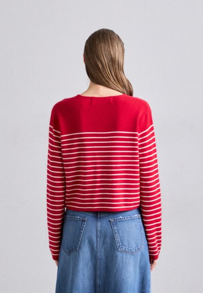 Rode gebreide trui met horizontale witte strepen, ronde halslijn en lange mouwen, gecombineerd met een blauwe denim rok met achterzakken.