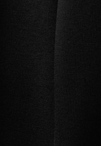 Tissu noir avec une texture en tricot fin, présentant des variations subtiles. Le matériau semble doux et légèrement extensible.