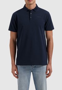 Marineblauwe polo-shirt gemaakt van zachte stof, beschikt over een klassieke kraag, drie knopen en een klein logo-detail op de borst.