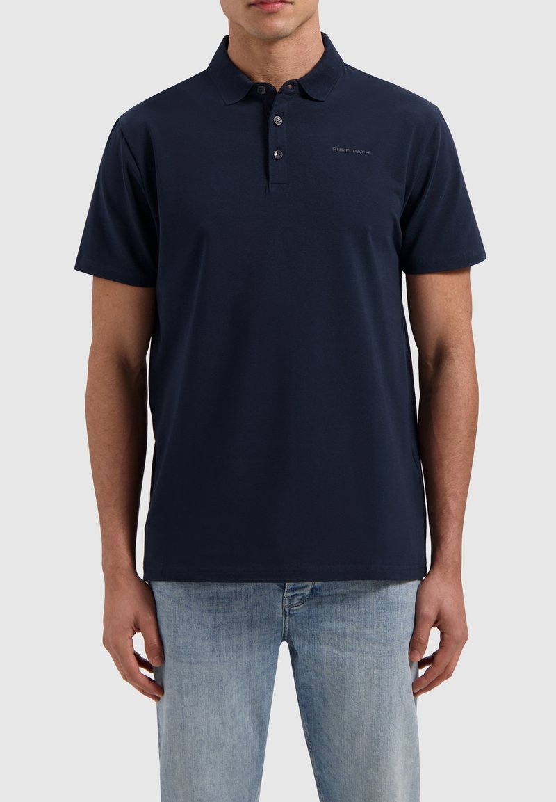 Marineblauwe polo-shirt gemaakt van zachte stof, beschikt over een klassieke kraag, drie knopen en een klein logo-detail op de borst.