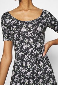 Robe noire à fleurs avec des manches courtes, présentant un décolleté rond, de petits motifs de fleurs roses et vertes, et une silhouette de jupe évasée.