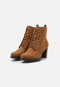 Bottines en daim marron avec un devant lacé, un bout pointu et un talon haut empilé. Tige texturée et détails de coutures horizontales sur les côtés.