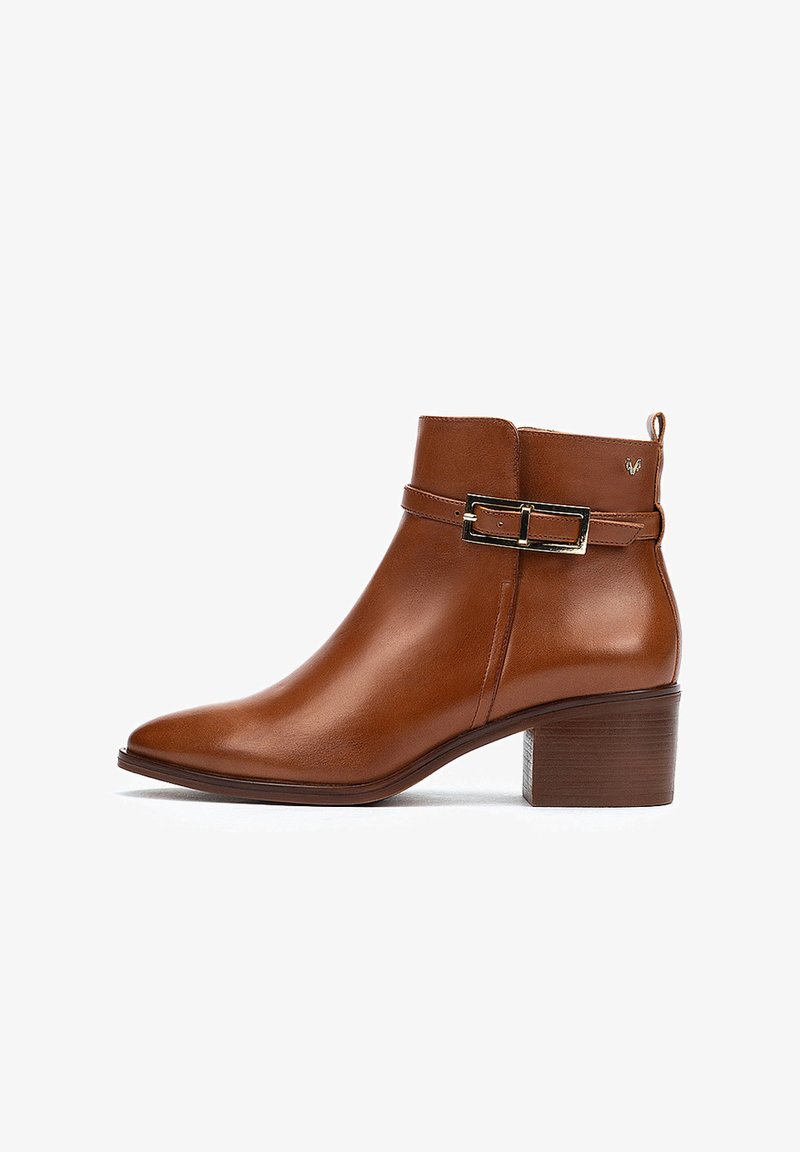 Bottine en cuir marron à bout pointu, avec un petit talon carré et un détail de boucle en or sur la sangle. Texture lisse, design épuré.