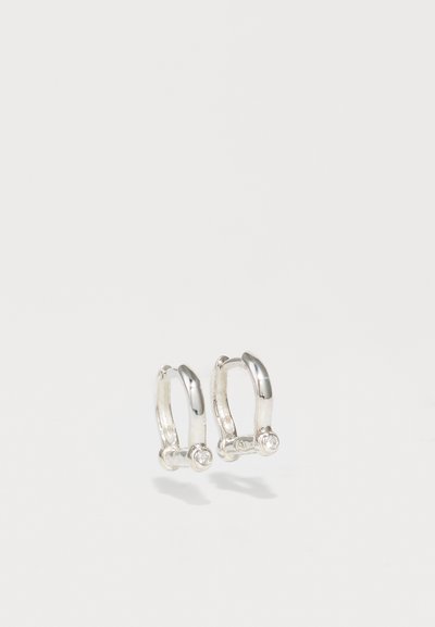 Boucles d'oreilles en argent en forme de hoop avec une finition lisse et polie, et un petit accent en pierre précieuse transparente sur la partie inférieure de chaque hoop.