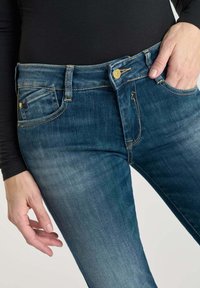 Jeans in donkerblauw denim met een klassiek vijf-pocket ontwerp, voorzien van gouden hardware en een lichte vervaging op de bovenbenen.