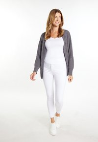 Cardigan grigio a maglia con un motivo testurizzato, indossato sopra una maglietta bianca aderente e pantaloni skinny bianchi, abbinato a sneaker bianche.