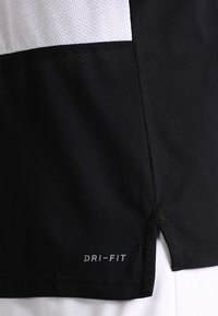 Maglietta sportiva nera con un pannello in rete bianco, logo Dri-FIT in argento, fessure laterali e una texture liscia con proprietà di assorbimento dell'umidità.