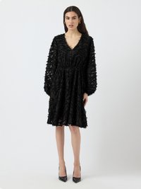 Black dress with long sleeves, V-neck, and gathered waist. Made of textured fabric with frayed detailing. Styled with black heels.