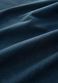 Tejido de algodón en un azul marino profundo, mostrando suaves pliegues y una textura lisa, con sutiles patrones de tejido que realzan su profundidad.