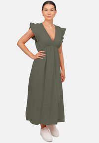 Robe verte olive, longueur genoux, avec des manches courtes à volants, décolleté en V, tissu texturé et taille ajustée. Portée avec des baskets blanches.
