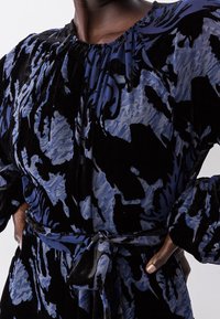 Robe à motif bleu et noir en velours doux, dotée d'un col froncé, de manches longues et d'une ceinture en tissu à la taille.