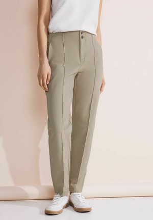 Pantaloni verde oliva chiaro con una texture liscia, taglio slim, pince frontali, due bottoni e tasche laterali, abbinati a sneaker bianche.